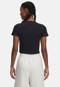 Black cropped t-shirt made from ribbed fabric with short sleeves, paired with high-waisted cream trousers, viewed from the back.