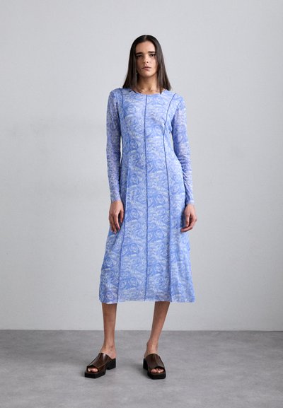 Robe bleu clair avec un motif floral, à manches longues et au design plissé. Portée avec des sandales à plateforme marron foncé. Texture de tissu lisse.