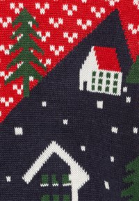 Sweter z dzianiny z czerwono-zielono-białym świątecznym wzorem, na którym znajdują się drzewa, domy i płatki śniegu na granatowym tle.