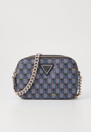 Kleine Guess crossbodytas met zwart, blauw en grijs geometrisch patroon en zilveren kettingriem op effen achtergrond.