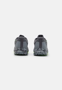 Pantofi sport gri cu o suprafață texturată, având o talpă cu model de camuflaj și accente verzi pe toc și talpă.