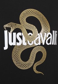 Svart tyg T-shirt med en intrikat design av en guldorm som är sammanflätad med texten "justcavalli" i vitt.