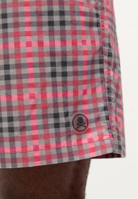Șorturi dintr-un material ușor, cu un model în carouri roșu, roz și gri. Include un buton transparent cu un design de skull și oase încrucișate.