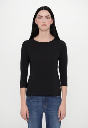 Schwarzes Langarmoberteil mit Rundhalsausschnitt und figurbetontem Design, aus einem glatten Stoff. Kombiniert mit blauen Jeans.