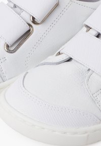 Weiße Sneaker mit einer strukturierten Leder- und glatten Textiloberfläche, doppelten Klettverschlüssen und weißen Gummisohlen.