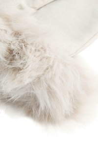 Faux pälsaccent i ljusbeige, mjuk och fluffig textur, kombinerad med en slät tygbakgrund som skapar ett lager-på-lager utseende.