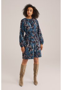 Rochie imprimată în nuanțe de teal cu un model floral, talie elastică și mâneci lungi, bufante. Asortată cu botine bej până la genunchi.