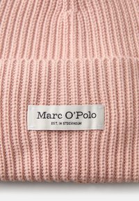 Gorro de punto en rosa claro con textura de canalé vertical y un dobladillo en la parte inferior. Presenta una etiqueta de tela blanca con "Marc O'Polo" y "EST. EN STOCKHOLM."