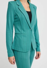 Blazer teal con righe verticali nere, chiusura a bottone singolo, forma sartoriale, rever a scantonatura e dettagli sulle tasche frontali.