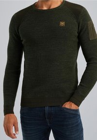 Maglione a coste verde oliva con colletto rotondo, polsini aderenti e una toppa utility sulla manica sinistra. Realizzato in un tessuto testurizzato.