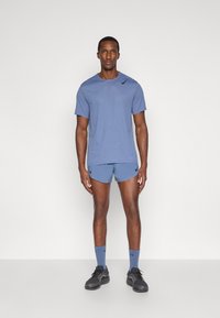 Abbigliamento sportivo da uomo composto da una maglietta a maniche corte di un blu chiaro con texture e pantaloni corti abbinati, completato da calzini blu e sneakers nere.