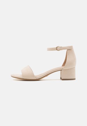 Sandale à talon bloc en daim beige avec bride de cheville, bout ouvert, large bande frontale et texture lisse. Design minimaliste avec un talon solide.