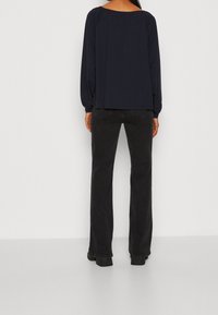 Navy long-sleeve top with a wide neckline and gathered back design, paired with black flared jeans and ankle boots.