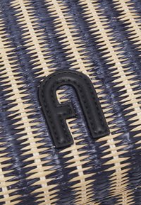 Texture de panier tissé bleu marine et beige avec une pièce en cuir noire cousue en forme de lettre "n" courbée et stylisée.