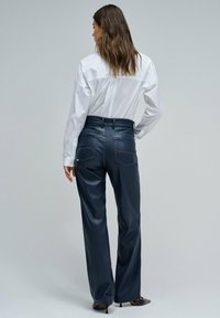 Pantalons en simili cuir bleu marine à taille haute, jambes droites et détails de poches arrière, associés à une chemise blanche à boutons.