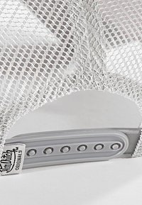 Casquette en maille argentée au design structuré, dotée d'une sangle réglable en plastique gris et d'une étiquette de marque. La maille présente un motif en grille.
