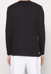 T-shirt noir à manches longues en coton doux. Coupe col rond et étiquette "Wet&Dry" discrète dans le bas du dos. Coupe ajustée.