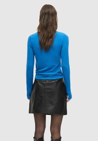 Blå langermet topp laget av stoff, kombinert med et svart skinnminiskjørt. Baksiden har en glatt finish og en tettsittende design.