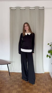 Haut à manches longues noir avec col blanc sur une couche blanche, associé à un pantalon noir à jambes larges ; se tient sur un sol en bois devant un rideau léger.