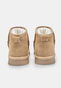 Hnědé semišové kotníkové boty s měkkou bílou vnitřní podšívkou, zesíleným podpatkem a plochou gumovou podrážkou. Vyznačují se minimalistickým designem s detailem šití.