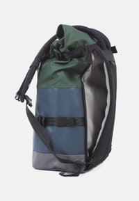 Vattentät ryggsäck med rulltoppsstängning. Har svarta, gröna och blå paneler, justerbara remmar och en grå inredning.