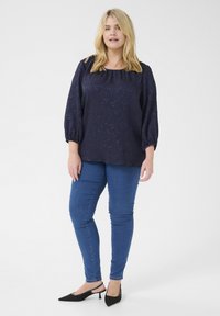 Blusa blu navy con motivo testurizzato e maniche a palloncino, abbinata a jeans slim fit e décolleté nere a punta.