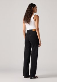 Zwarte high-waisted jeans met een recht gesneden ontwerp, voorzien van een logo patch op de achterkant. De stof heeft een gladde textuur en minimale details.