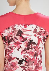 Top deportivo rojo de mangas cortas, con un estampado floral en tonos rosa y burdeos en la parte posterior. Tejido texturizado que absorbe la humedad.