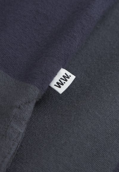 Katoenen stof in donker marineblauw en steenkoolgrijs, met een subtiele textuur. Een klein wit label met zwarte tekst is zichtbaar.