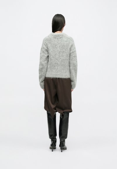 Szary, futrzasty sweter z szerokim kołnierzem, w połączeniu z brązowymi, luźnymi spodniami oraz czarnymi, wysokimi botkami za kolano. Teksturowany materiał i warstwowy styl.