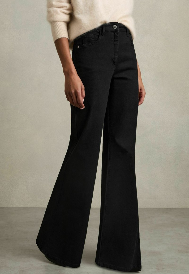 Jean flare noir en denim, avec une taille haute et une fermeture à boutons, présentant une texture lisse et des lignes épurées.
