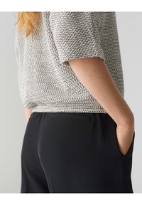 Schwarze Hose mit glatter Textur, kombiniert mit einem kurzärmeligen, strukturierten Oberteil mit einem schwarz-weißen Karomuster.