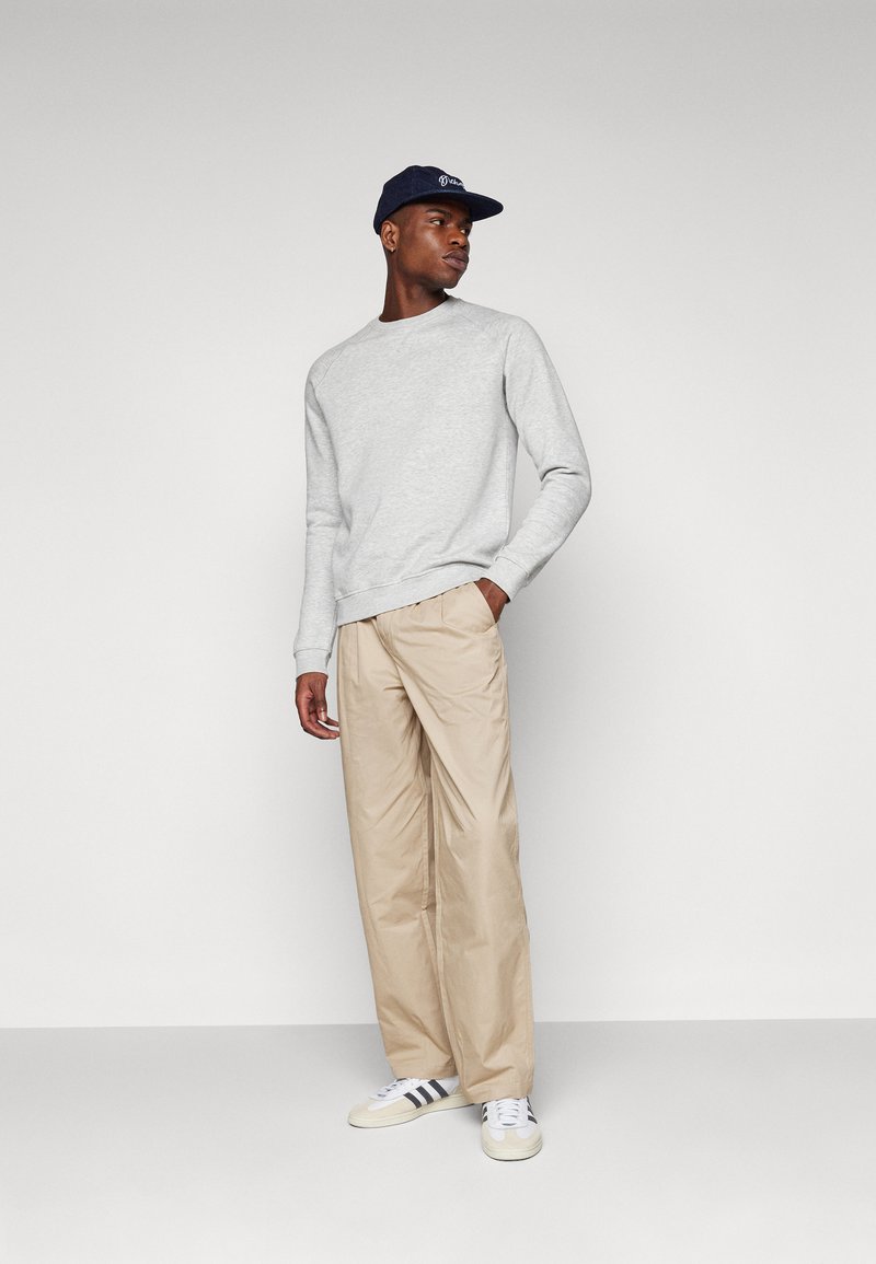 Suéter gris de manga larga, pantalones beige con pliegues, zapatillas blancas con rayas negras y una gorra azul marino con un logo. Textura de tela suave.