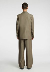 Beżowy garnitur z dopasowaną marynarką i spodniami o szerokich nogawkach, charakteryzujący się subtelną fakturą i rozcięciem z tyłu, uzupełniony czarnymi butami.
