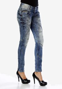 Jean skinny en denim bleu délavé, présentant un design ajusté, des coutures décoratives et une taille mi-haute. Assortis avec des escarpins noirs brillants.