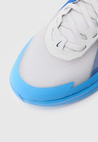 White and light blue sneaker with a textured mesh upper, rounded toe, padded sole, and plastic accents near the laces.