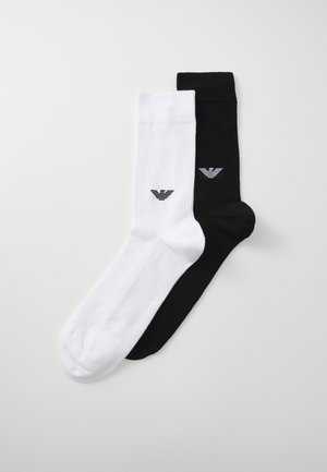 Calcetines de algodón en blanco y negro con textura acanalada. Cada calcetín tiene un logo en el tobillo. El calcetín blanco tiene un logo negro; el calcetín negro tiene un logo blanco.