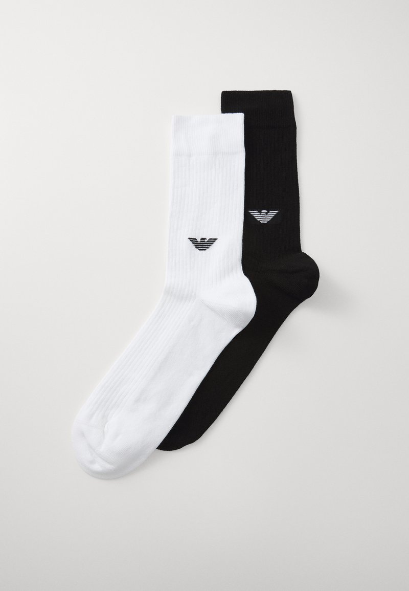 Socks de algodão em preto e branco com textura canelada. Cada par de meias apresenta um logo no tornozelo. A meia branca tem um logo preto; a meia preta tem um logo branco.