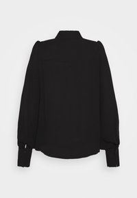 Blouse noire à manches longues avec col montant, poignets boutonnés et épaules légèrement bouffantes, vue de dos sur un fond uni.