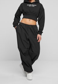 Svart kort hoodie med logotyp, i kombination med lösa svarta byxor med elastisk midja. Vita sneakers fulländar outfiten.