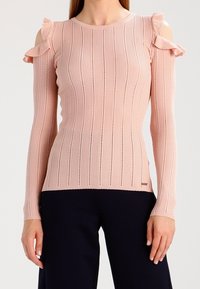 Top a maniche lunghe con spalle scoperte in rosa chiaro, con righe verticali, dettagli a taglio e balze sulle spalle.