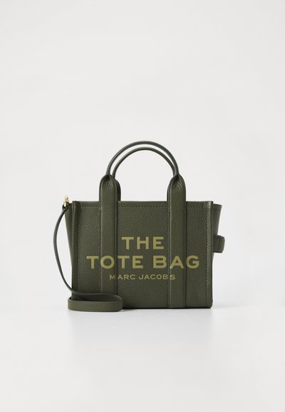 Sac fourre-tout en cuir texturé vert foncé avec deux poignées, une bandoulière amovible et l'inscription dorée "THE TOTE BAG MARC JACOBS" à l'avant.