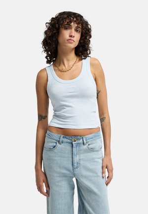 Jasnoniebieski bawełniany top na ramiączkach o dopasowanym kroju, szerokich ramiączkach i wyhaftowanym logo na środku. Połączony z luźnymi jasnoniebieskimi jeansami.