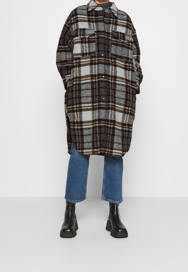 Camicia di flanella a quadri grigia, nera e gialla, con chiusura a bottoni, due tasche sul petto e una vestibilità rilassata e oversize.