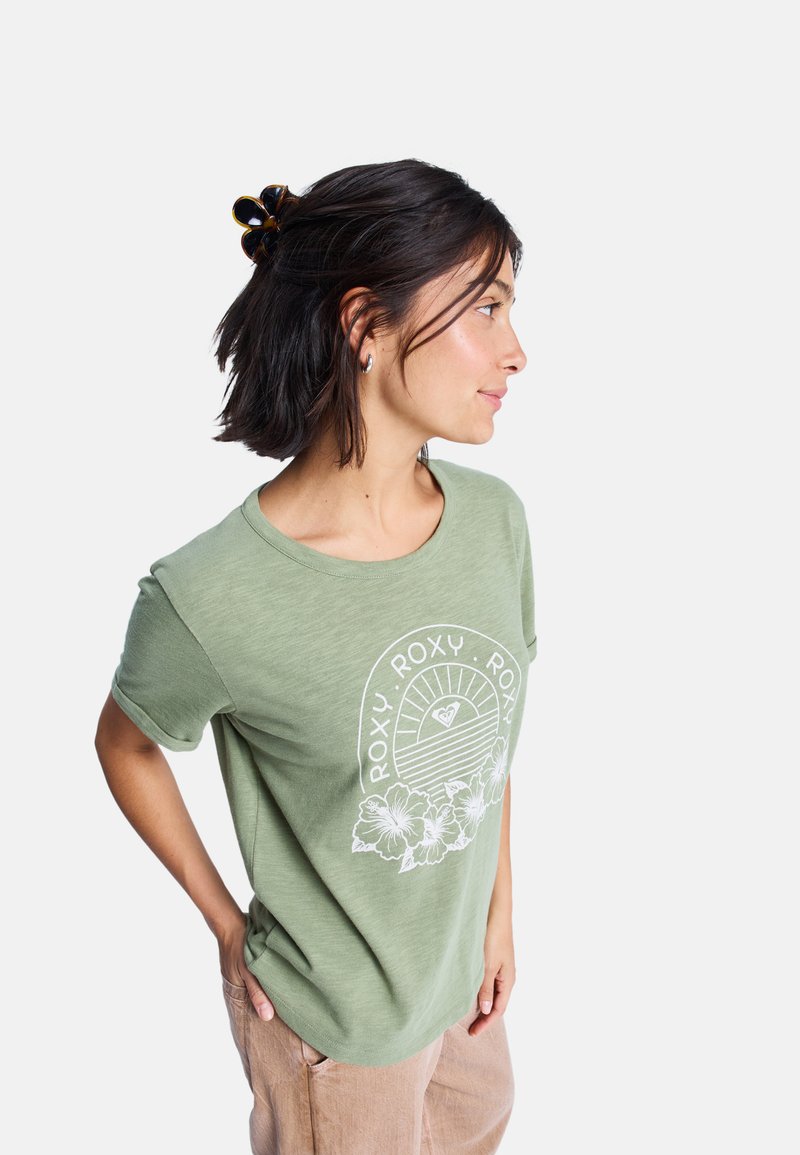 T-shirt vert à manches courtes avec un graphique floral blanc et le texte "ROXY". Fabriqué en matériau léger, il présente une coupe décontractée et un col rond.