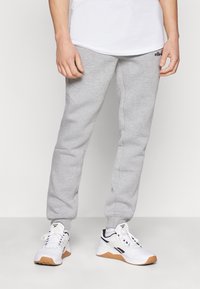 Grå joggebukser laget av myk stoff, med en innsnittet passform, elastiske mansjetter, og en liten svart logo på midjebåndet.
