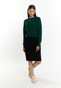 Maglione verde a trecce, gonna a tubino nera e sneakers gialle. Incentrato su fibre texturizzate e colori a contrasto in un look casual.