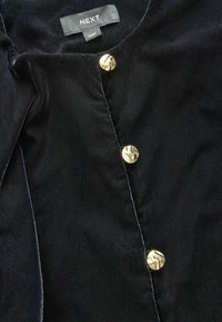 Marineblaues, strukturiertes Stoffbluse mit rundem Ausschnitt, ausgestattet mit drei metallischen goldenen Knöpfen an der Vorderseite. Markenetikett sichtbar.
