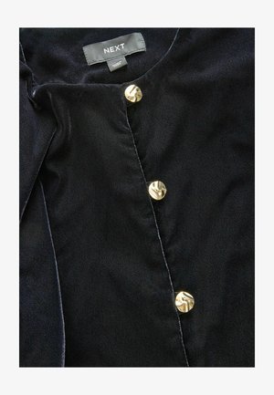 Tmavě modrá bluzka z texturované látky s kulatým výstřihem, na přední straně se třemi kovovými zlatými knoflíky. Viditelná značka.