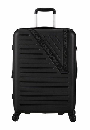 Maleta rígida negra con superficie acanalada, asa telescópica y cuatro ruedas. Presenta el logo de "American Tourister" en la parte frontal.